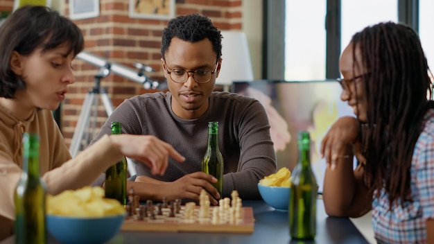 Portrait of african american man playing chess game with friends in living room, having fun with board games and alcoholic drinks. Male person hanging out with cheerful people for entertainment.