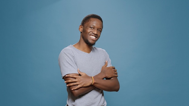 Portrait of african american man posing with arms crossed on camera in studio. Young man smiling and feeling confident, having casual positive expression, ambitious male model.