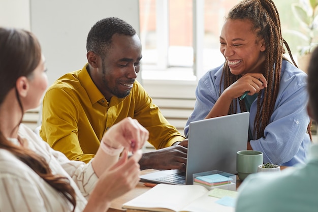 Portrait of African-American man and woman laughing cheerfully while working on team project with multi-ethnic group of people