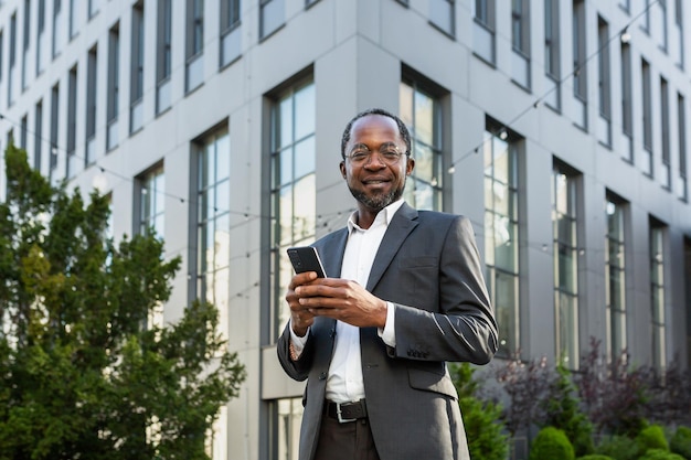 Portrait of african american mature businessman senior man outside office building holding phone in