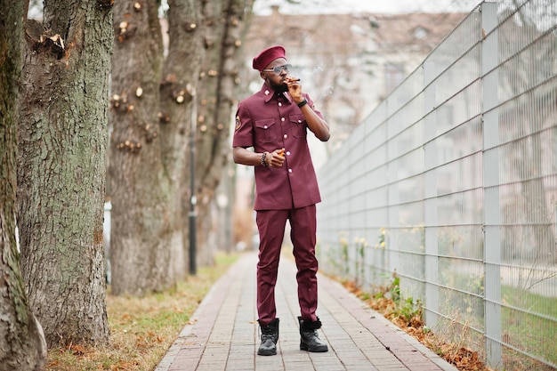 Portrait of African American military man in red uniform, sungalasses and beret. Captain smoke cigar.