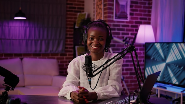 Photo portrait of african american podcaster sitting at desk in home recording studio with boom arm microphone and digital audio mixer. online radio host smiling confident at camera while broadcasting live.