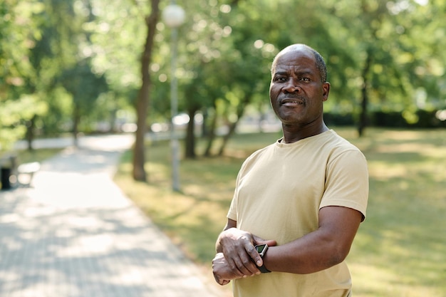 Photo portrait of african american senior man with fitness smartwatch looking at camera standing in the park