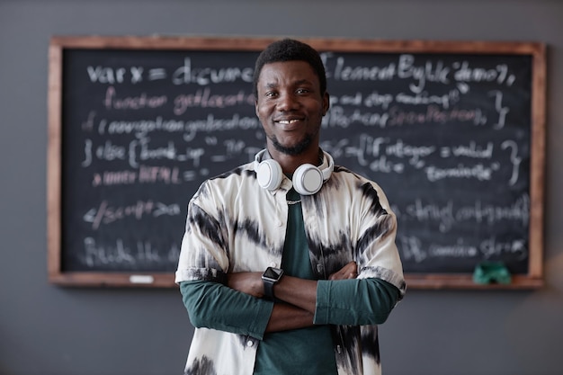 Portrait of African American teacher smiling at camera while standing with his arms crossed with blackboard in background