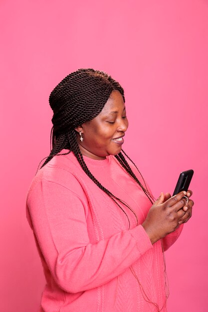 Portrait of african american woman holding mobile phone browsing on internet, watching funny video on smartphone relaxing during leisure time. Model posting picture on social media