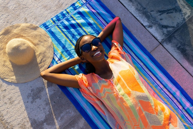 수건에 누워 정원 수영장 옆에서 일광욕을 하는 아프리카계 미국인 여성의 초상화. 라이프 스타일, 자유 시간 및 휴가, 여름, 햇빛, 변함 없음.
