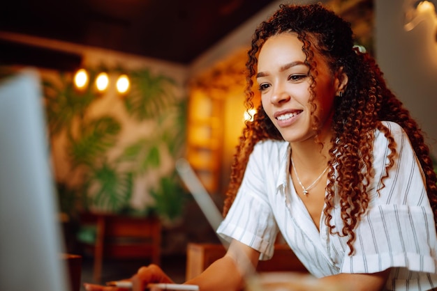 Portrait of African American woman sitting at cafe having video call on laptop computer