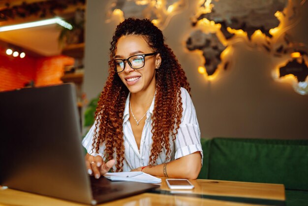 Portrait of African American woman sitting at cafe having video call on laptop computer