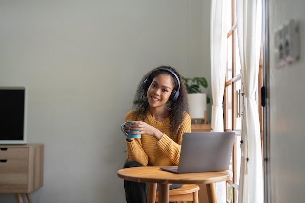 Portrait of African American woman talking on video conference call using laptop and headphones taking notes on notepad Brunette sits at table in home office