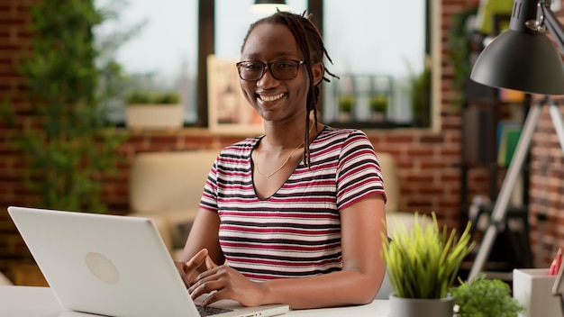 Ritratto di donna afroamericana che utilizza il laptop alla scrivania, lavorando in remoto su attività di avvio. svolgere lavoro freelance a distanza su computer da casa, tecnologia di lavoro a distanza e rete online.