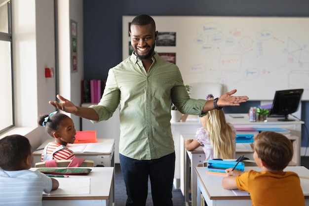 Foto ritratto di un giovane insegnante afroamericano che fa gesti mentre si trova accanto agli studenti in classe