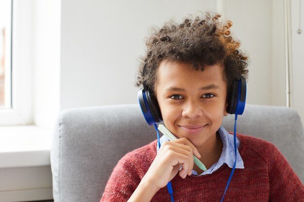 Portrait of African boy with curly hair in headphones listening to music and smiling