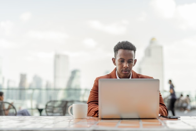 Portrait of African businessman outdoors in coffee shop using laptop computer