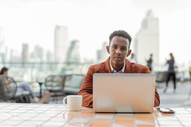 Portrait of African businessman outdoors in coffee shop using laptop computer