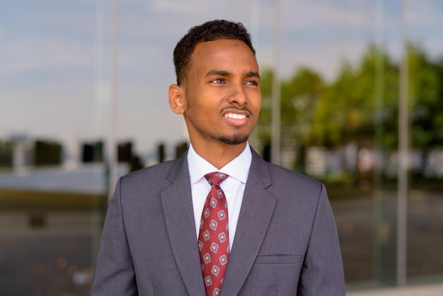 Portrait of African businessman wearing suit and tie outdoors in city while smiling and thinking