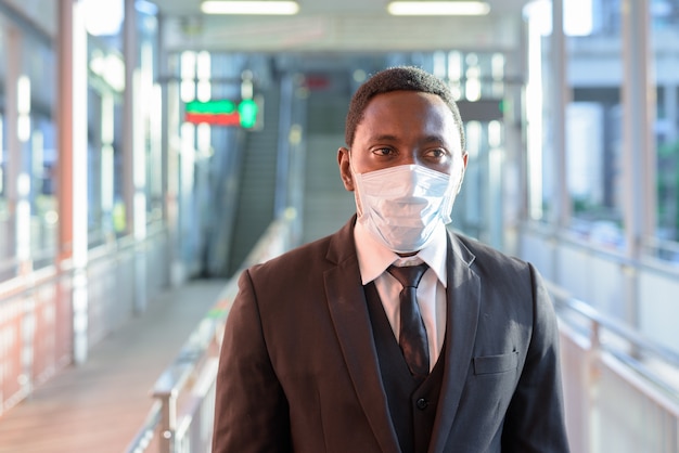 Portrait of African businessman with mask thinking at the train station outdoors