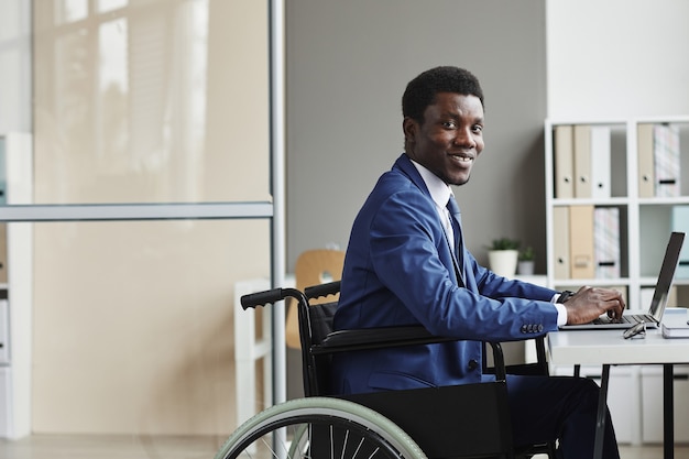 Ritratto di uomo d'affari africano disabile sorridente durante la digitazione sul computer portatile in ufficio