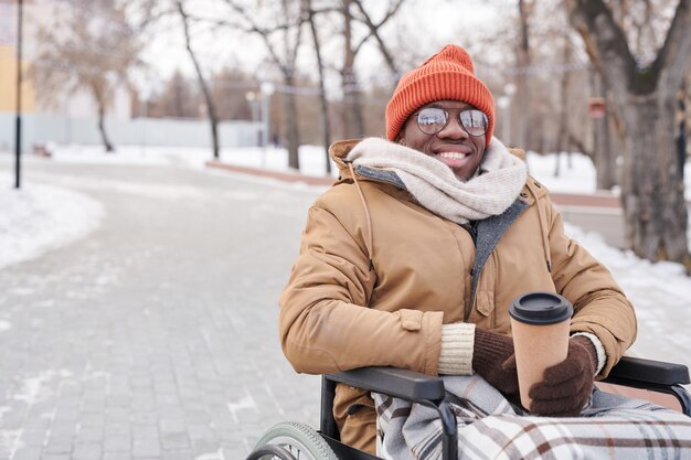 公園でホットコーヒーを飲みながらカメラに微笑んで車椅子のアフリカの障害者の肖像画