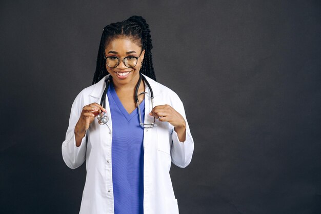 portrait of african female doctor in scrub and lab coat with stethoscope against white background