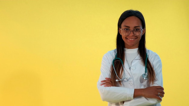 Portrait of african female doctor smiling to the camera on yellow background she is lab coat and wit...