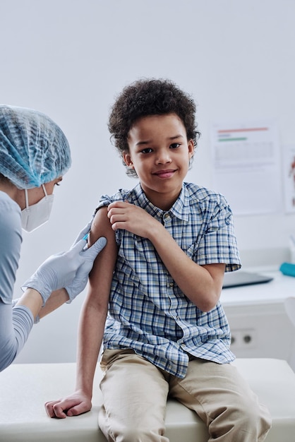 Portrait of african little boy smiling at camera while nurse giving injection in his arm at procedur