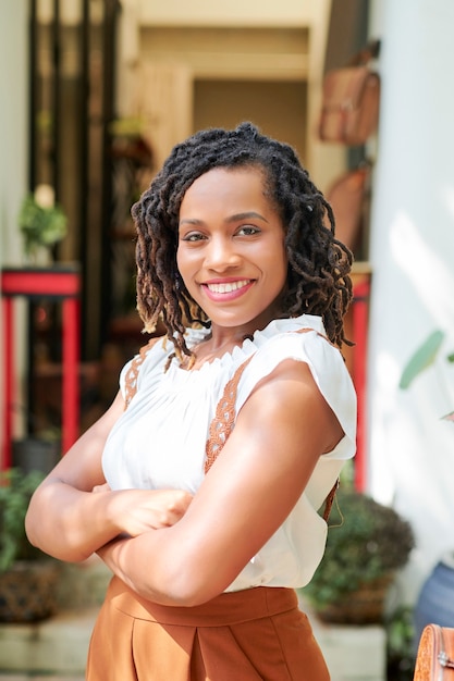 Portrait of African pretty woman smiling at camera while standing with her arms crossed in the city outdoors