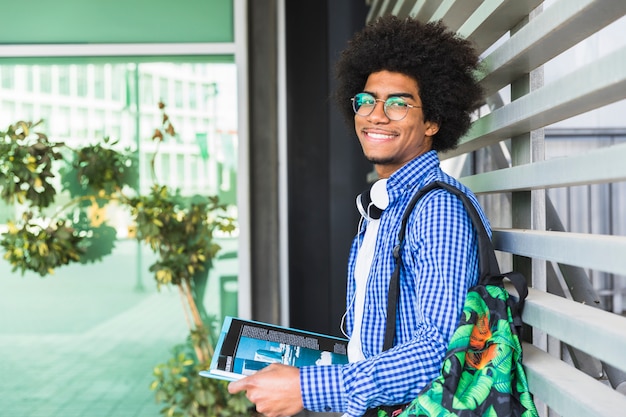 Portrait of an african smiling male student leaning on wall