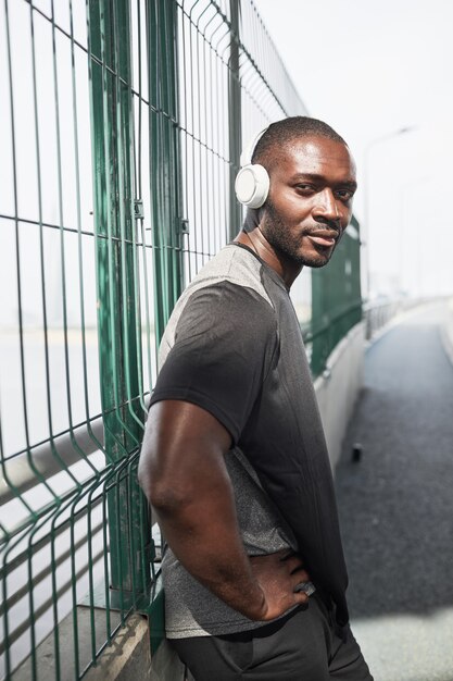 Portrait of african young athlete looking at camera while training in wireless headphones on the sta...