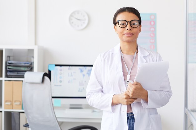 Photo portrait of african young female doctor in white coat while standing at office