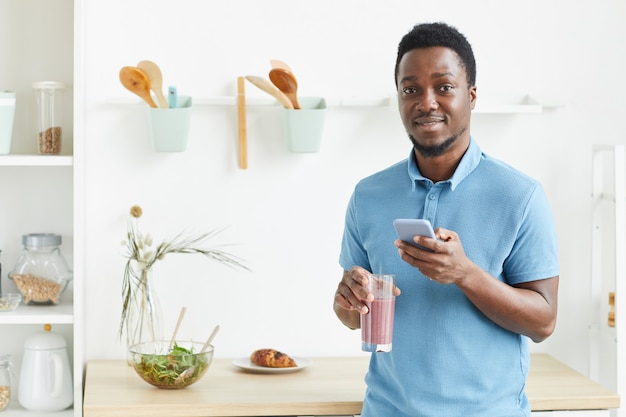 Portrait of African young guy smiling and drinking fresh cocktail in the morning at home