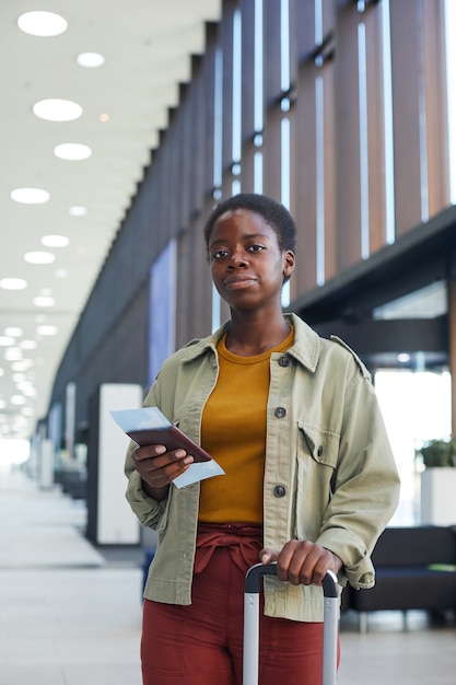 Portrait of African young woman standing with luggage and holding airplane tickets she looking  at the airport