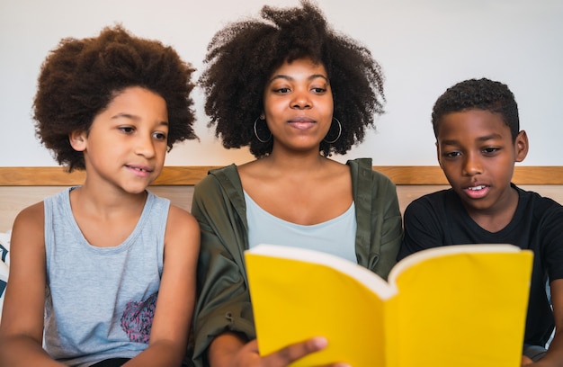 Portrait of Afro American mother reading a book to her children at home. Family and lifestyle concept.