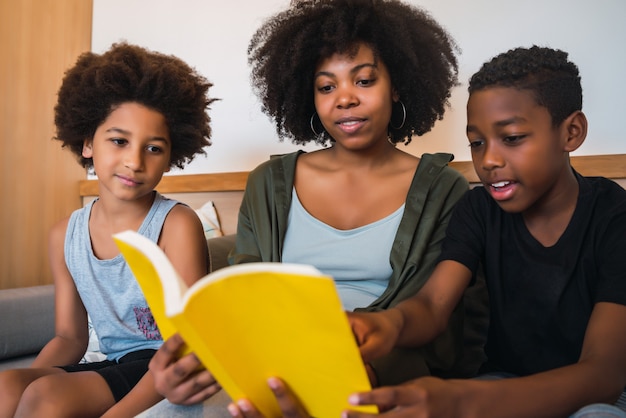 Ritratto della madre afroamericana che legge un libro ai suoi figli a casa. concetto di famiglia e stile di vita.