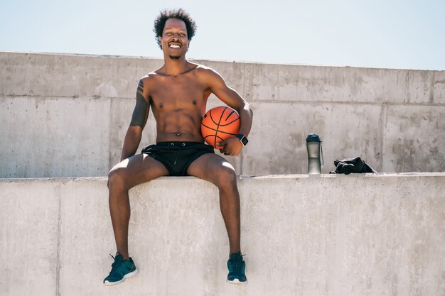 Portrait of afro athlete man holding a basketball ball while sitting outdoors