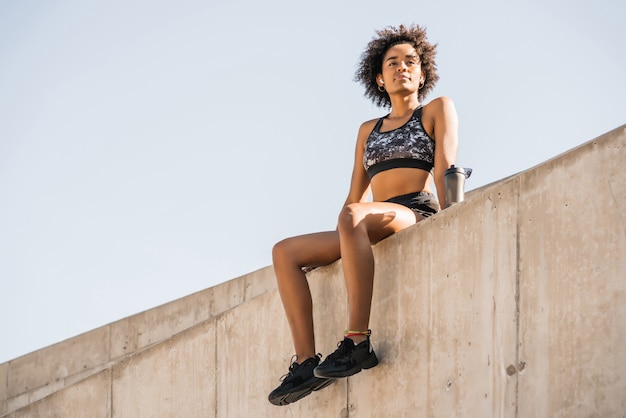 Portrait of afro athlete woman relaxing and sitting after work out outdoors. Sport and healthy lifestyle.