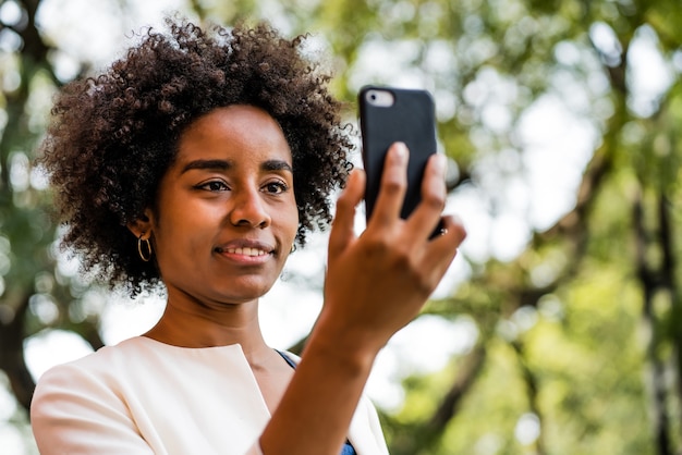 公園で屋外に立っている間携帯電話でビデオ通話をしているアフロビジネス女性の肖像画