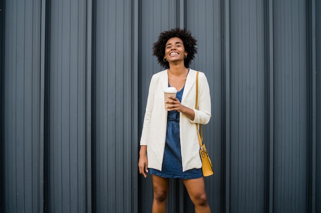 Portrait of afro business woman holding a cup of coffee while standing outdoors on the street