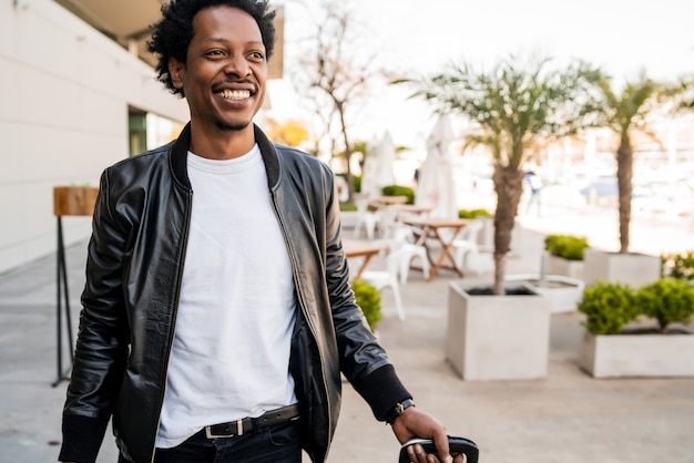 Portrait of afro tourist man carrying suitcase while walking outdoors on the street. Tourism concept.