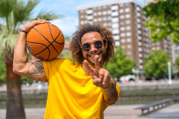 Portrait of an afrohaired man in a yellow tshirt with a basketball ball Portrait in the city smiling on summer vacation