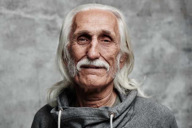 Foto ritratto di pensionato uomo caucasico dai capelli grigi invecchiato. cool nonno con i baffi e la faccia gentile sorridente che guarda l'obbiettivo su sfondo grigio