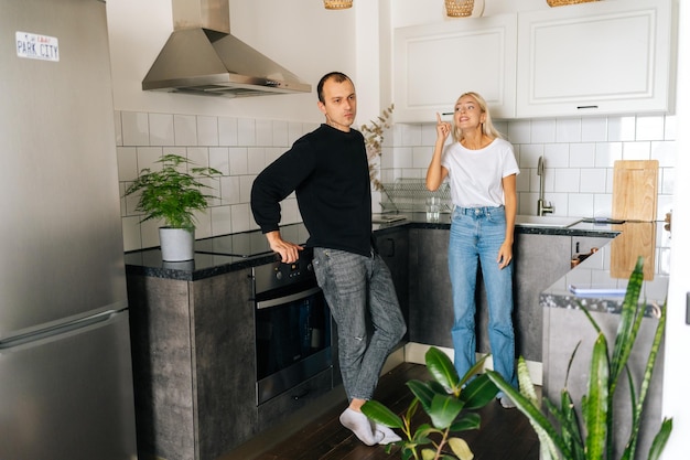 Portrait of aggressive emotional blonde wife scolding raising voice shouting at ignoring tired husband standing in kitchen room looking away