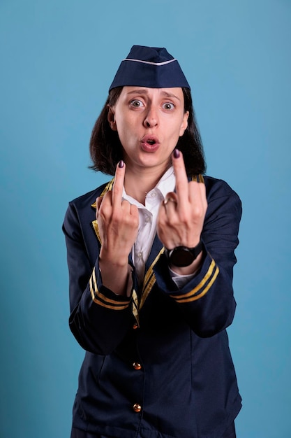 Portrait of aggressive furious stewardess showing middle finger\
offensive gesture. angry flight attendant in professional aviation\
uniform demonstrating provocative rude behavior