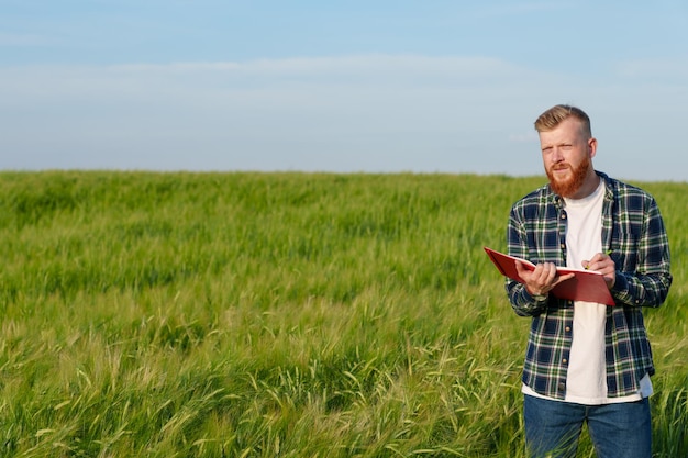 Portrait of an agronomist with a notebook in a wheat field a\
farmer with a beard and a shirt prepares the field for the future\
harvest