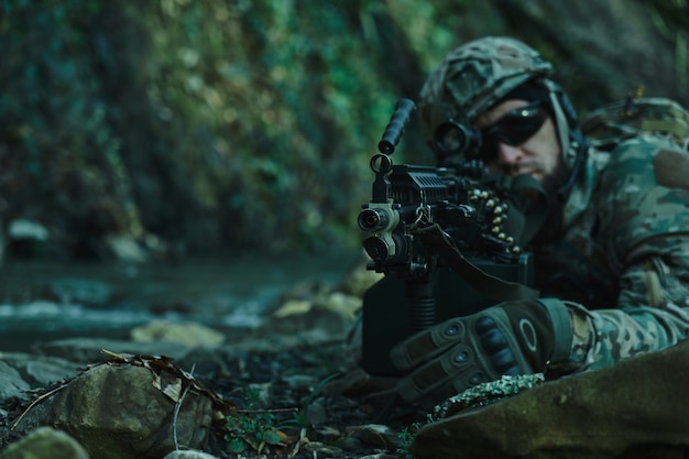 Ritratto di giocatore di softair in attrezzatura professionale in casco che mira alla vittima con la pistola nella foresta. soldato con armi in guerra