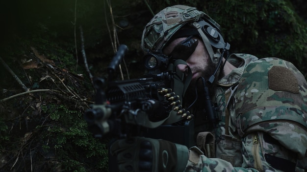 Photo portrait of airsoft player in professional equipment in helmet aiming at victim with gun in the forest. soldier with weapons at war