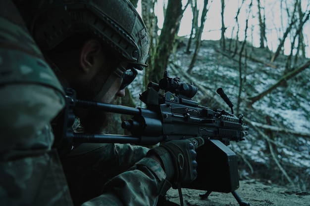 Portrait of airsoft player in professional equipment in helmet aiming at victim with gun in the forest. Soldier with weapons at war