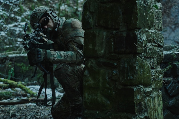 Portrait of airsoft player in professional equipment in helmet
aiming at victim with gun in the forest. soldier with weapons at
war