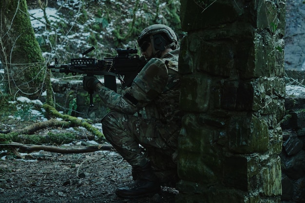 Portrait of airsoft player in professional equipment in helmet aiming at victim with gun in the forest. Soldier with weapons at war