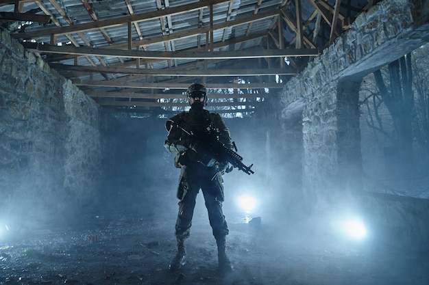Portrait of airsoft player in professional equipment with\
machine gun in abandoned ruined building. soldier with weapons at\
war