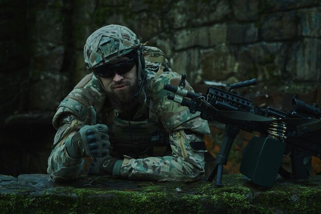 Portrait of airsoft player in professional equipment with\
machine gun in the forest. soldier with weapons at war